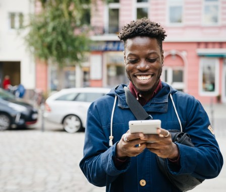 Man smiling and typing on smartphone outside