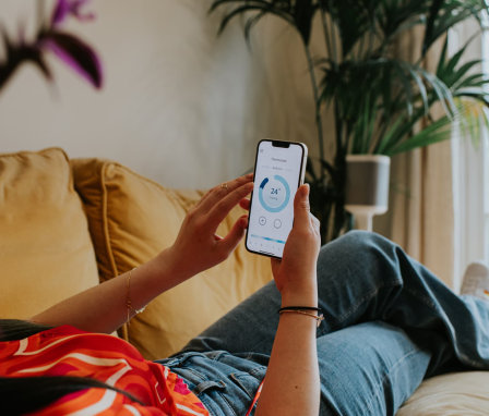 Woman laying on couch adjusting thermostat on iPhone